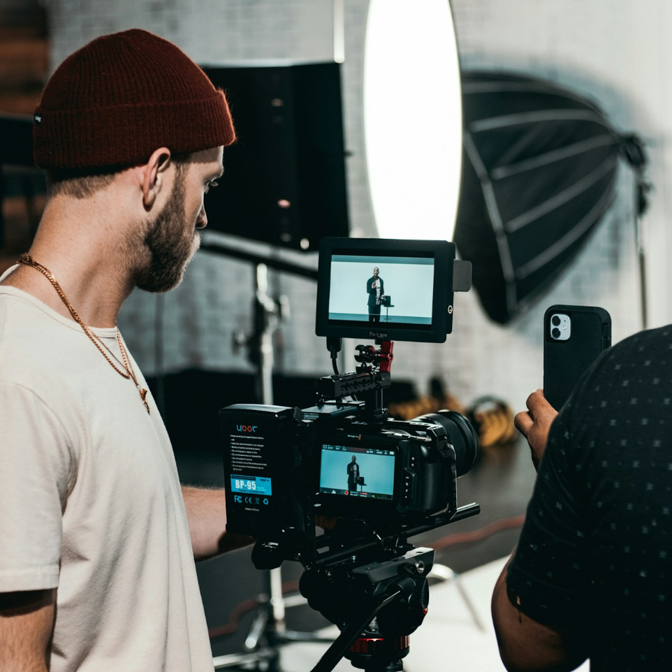 man in white polo shirt standing in front of black video camera